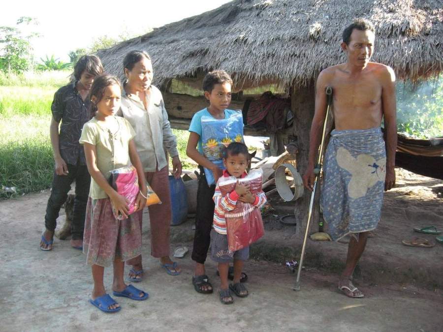 Family receiving aid packages outside their thatched home