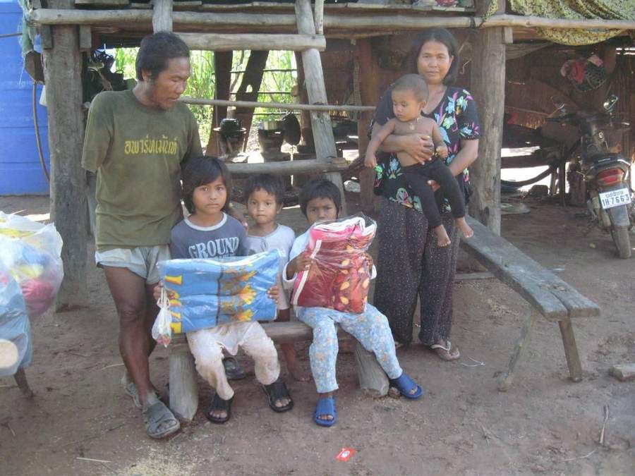 Family sitting on bench outside their thatched-roof house