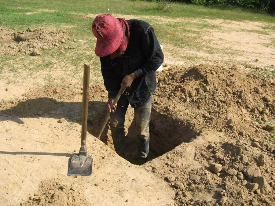 Worker digging deep hole with shovel in dry ground