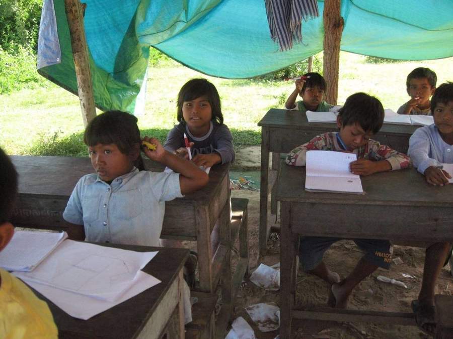 Children studying at wooden desks under blue tarp shelter