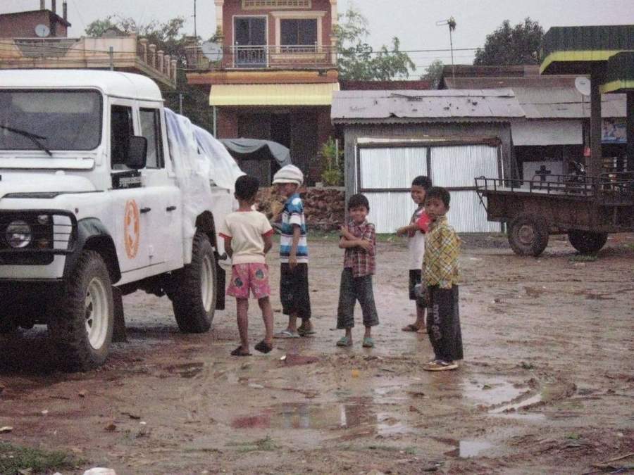 Children standing near GSO vehicle in muddy village street