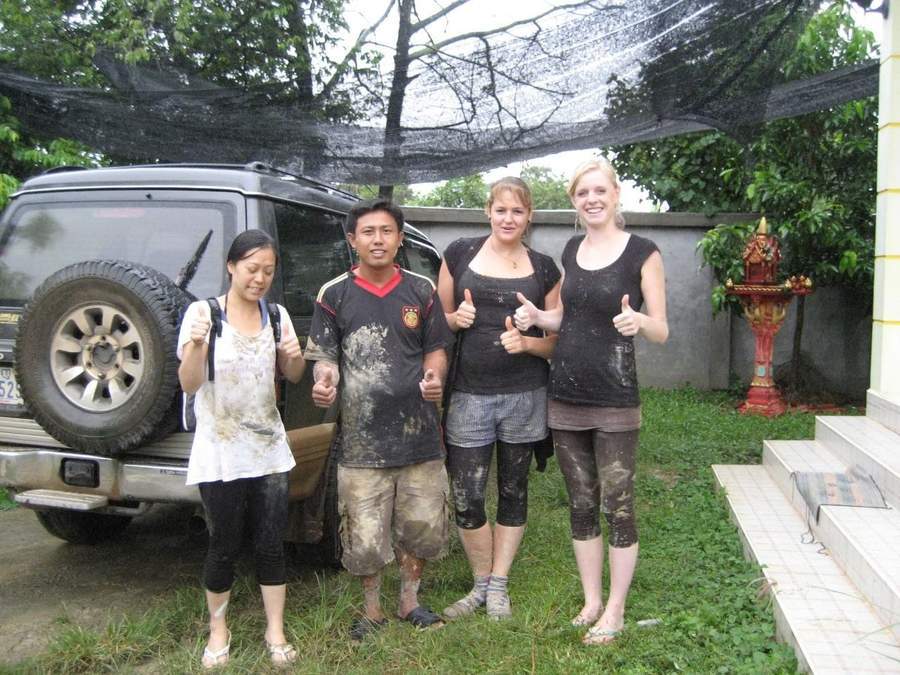Four muddy volunteers giving thumbs up beside SUV