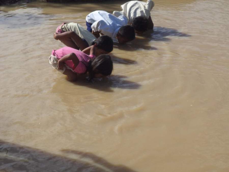 Children and adult wading in muddy river water