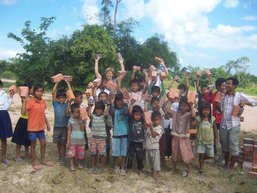 Group of children holding bricks up in the air with volunteers