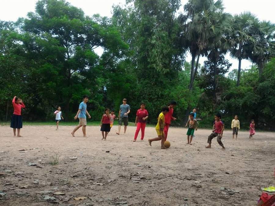 Group of children and adults playing soccer on dirt field