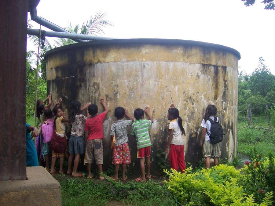 Children touching large concrete water tank with rainwater pipe