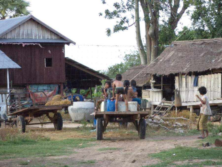 Children standing on cart in village with wooden houses