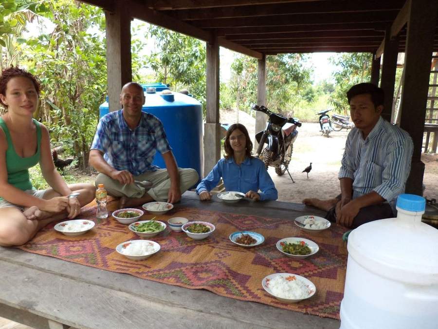 Group sitting on mat eating rice meal with blue water tank