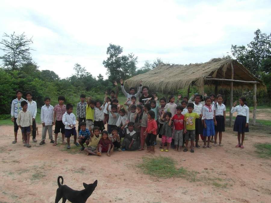 Large group of children and volunteer at thatched-roof shelter