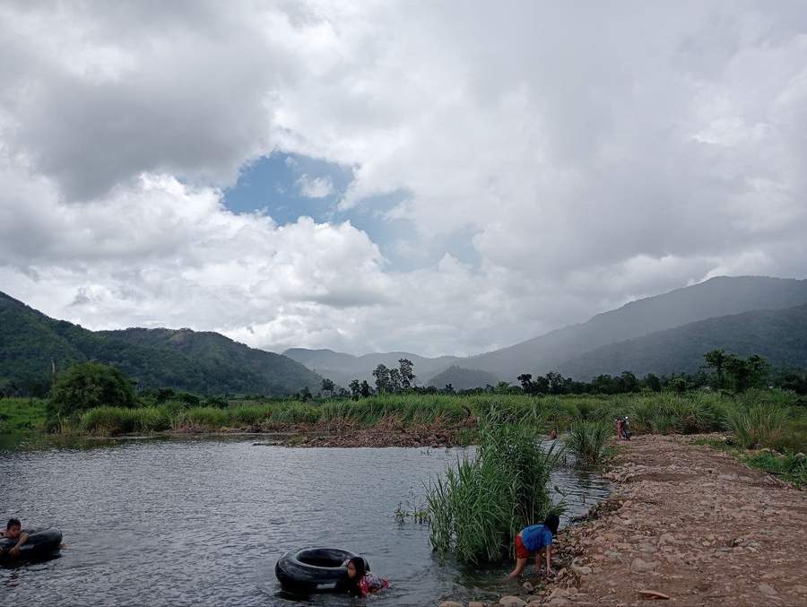 Children swimming with inner tubes in river with mountain backdrop