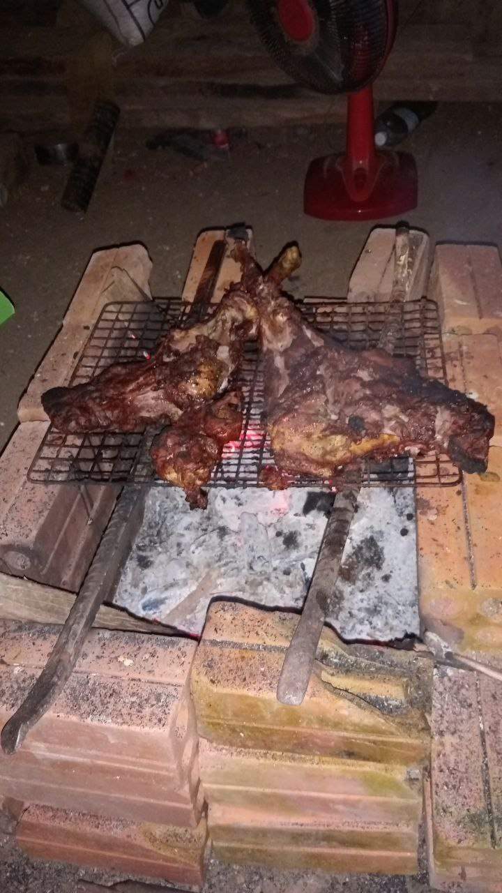 Meat roasting on brick grill over charcoal fire