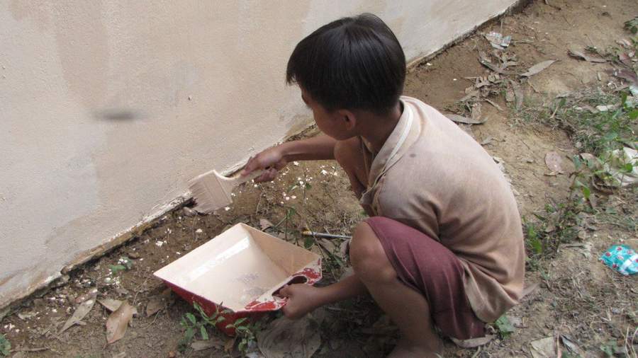 Young boy crouching painting wall with brush