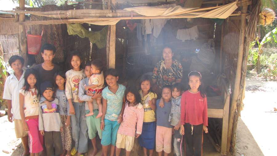Large family standing in front of thatched-roof hut