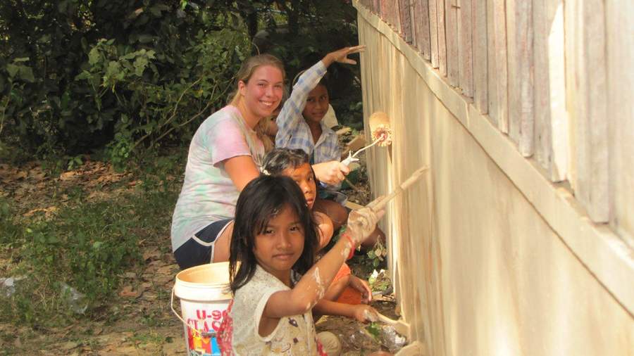Volunteers and children painting wall of building with brushes
