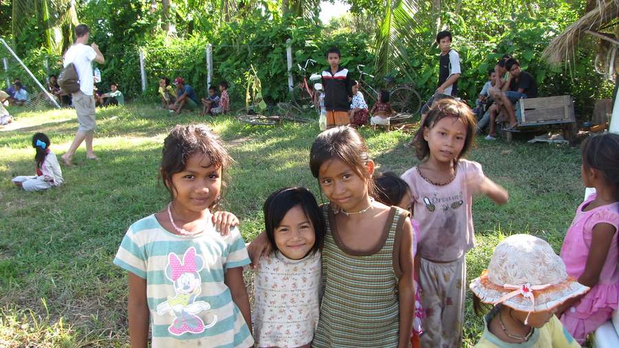 Four girls posing together in grassy field with village behind
