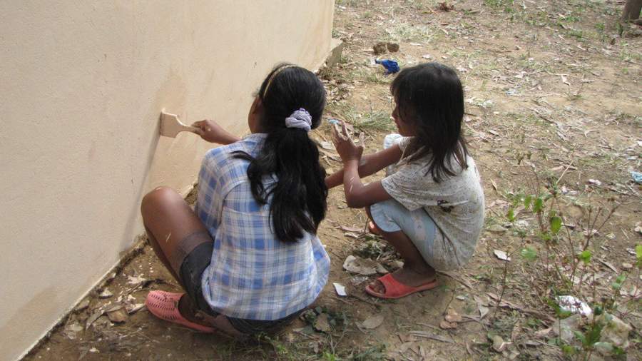 Two girls painting wall with brushes in village