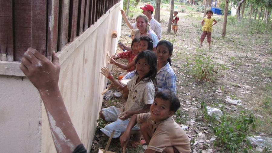 Volunteers and children painting wall of building together