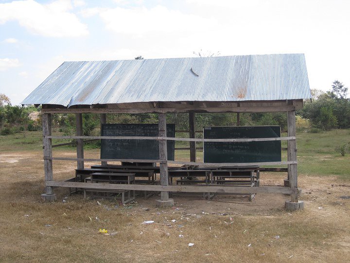 Open-air wooden classroom shelter with blackboards and desks