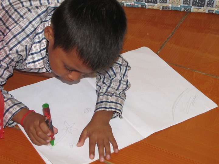 Child drawing on white paper with green marker on floor