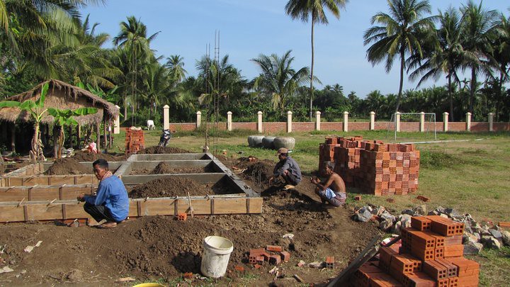Men working on brick foundation with piles of dirt and bricks