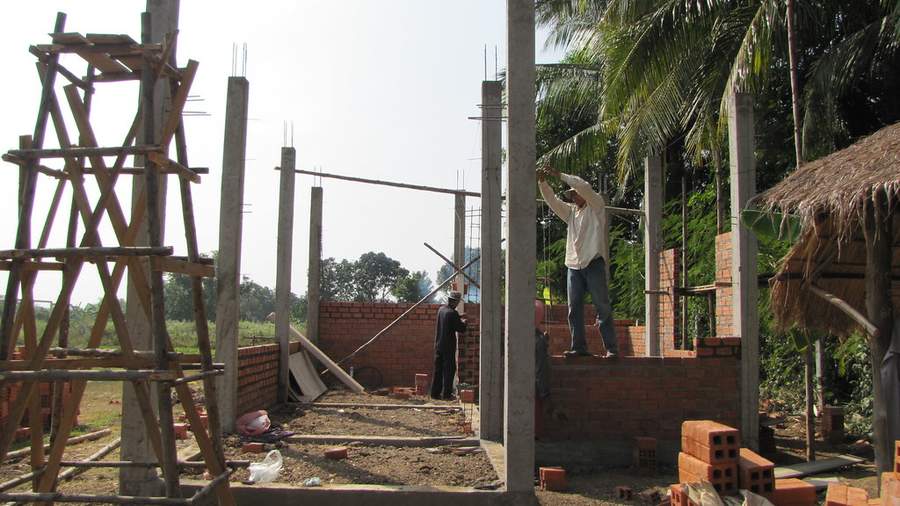 Workers building brick walls with concrete pillars and scaffolding