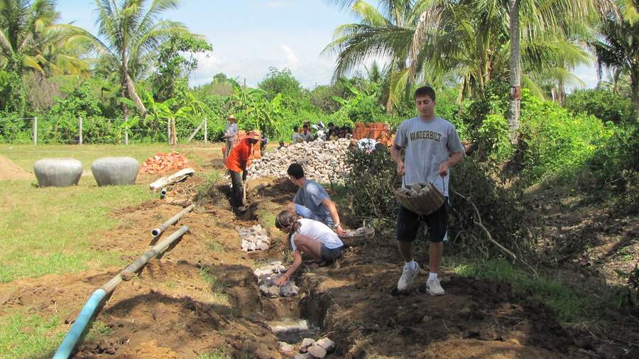 Volunteers working in trench laying pipes with rocks