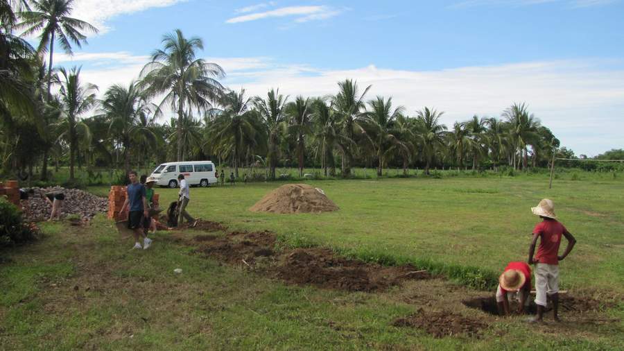 Workers digging in grassy field with palm trees and van