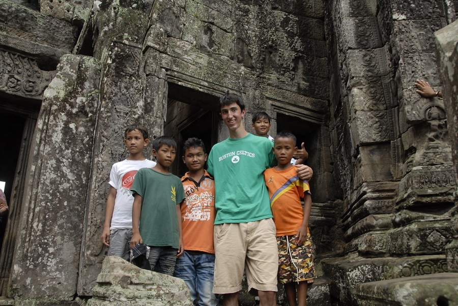 Young man in green shirt with Cambodian children at ancient temple