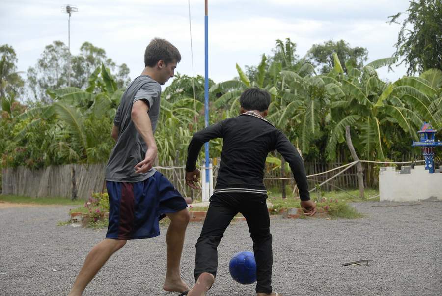 Volunteer and local boy playing soccer on gravel court