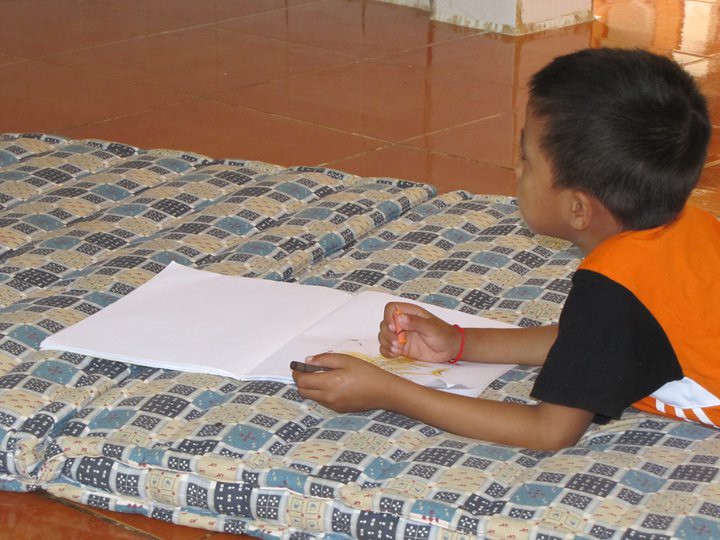 Young boy lying on bed drawing in notebook