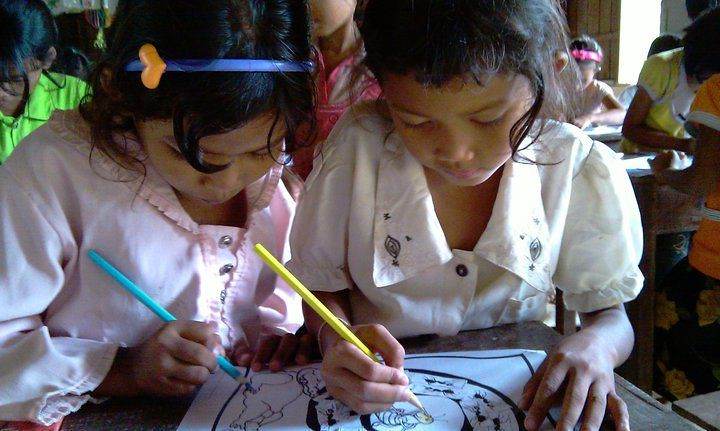 Two young girls coloring pictures together at desk