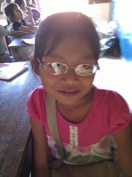 Young girl in pink shirt with glasses smiling in classroom