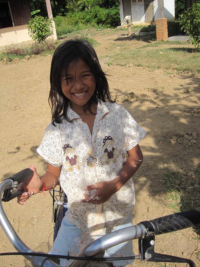 Smiling young girl standing with bicycle in village