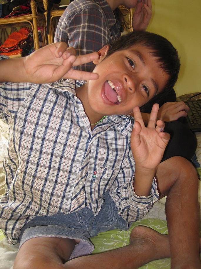 Boy making peace signs sitting on bed