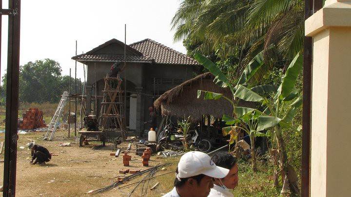 Building under construction with scaffolding palm trees and thatched-roof shelter
