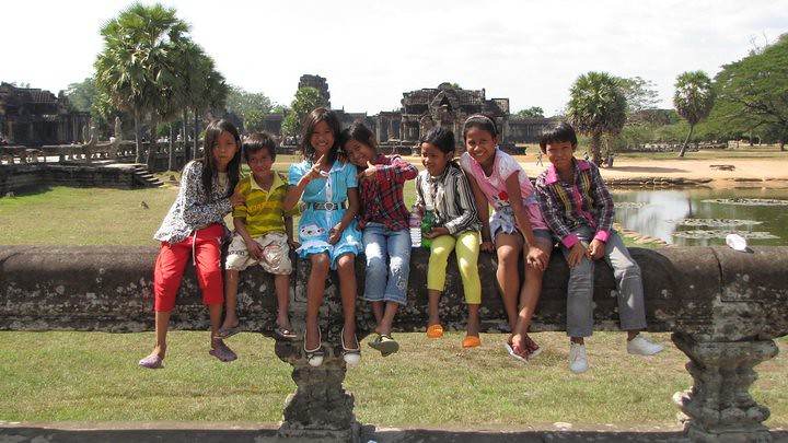 Children sitting on stone wall with ancient temple ruins and pond