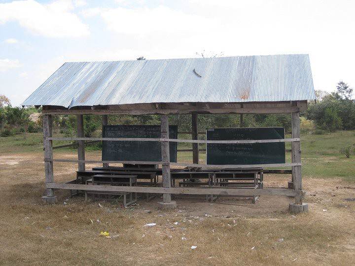 Open-air wooden schoolhouse with tin roof and blackboards