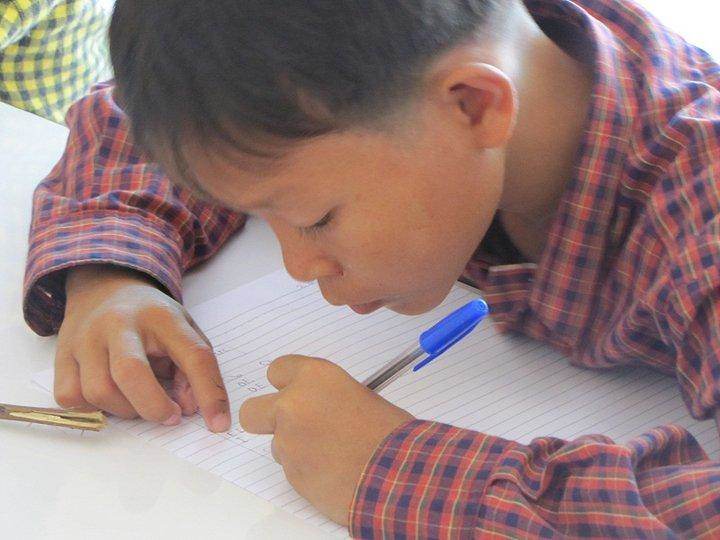 Close-up of boy writing in notebook with blue pen