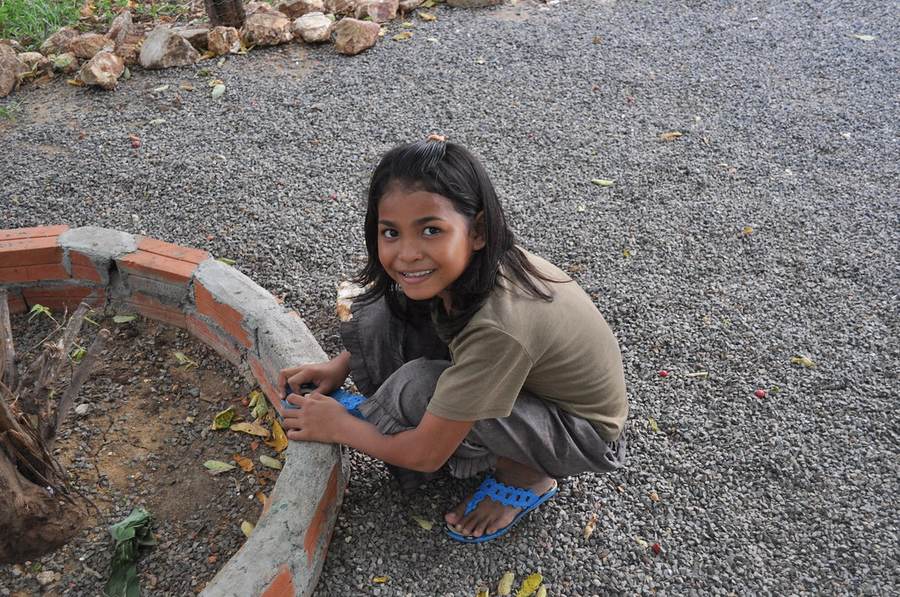 Girl crouching next to brick garden border