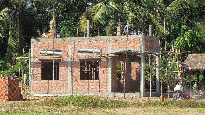 Brick building under construction with scaffolding and palm trees