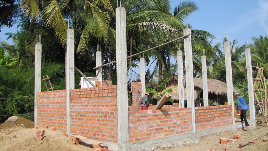 Brick building under construction with concrete pillars and palm trees