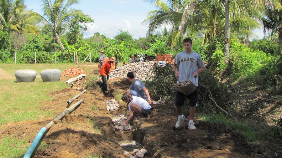 Volunteers working in trench laying pipes with rocks