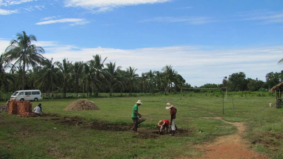 Workers digging on grass field with brick piles and white van
