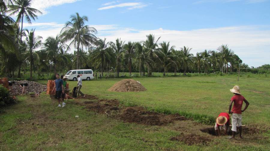 Workers digging on grass field with brick piles and palm trees