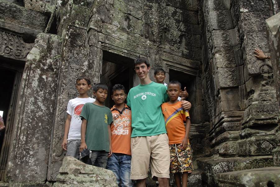 Young man in green shirt with Cambodian children at ancient temple