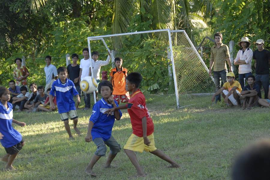 Children playing soccer near goal with spectators